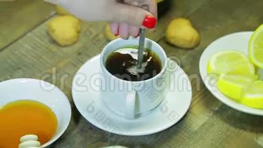 女人在木桌上的白色杯子里搅拌勺子。 新鲜冲泡的红茶..
